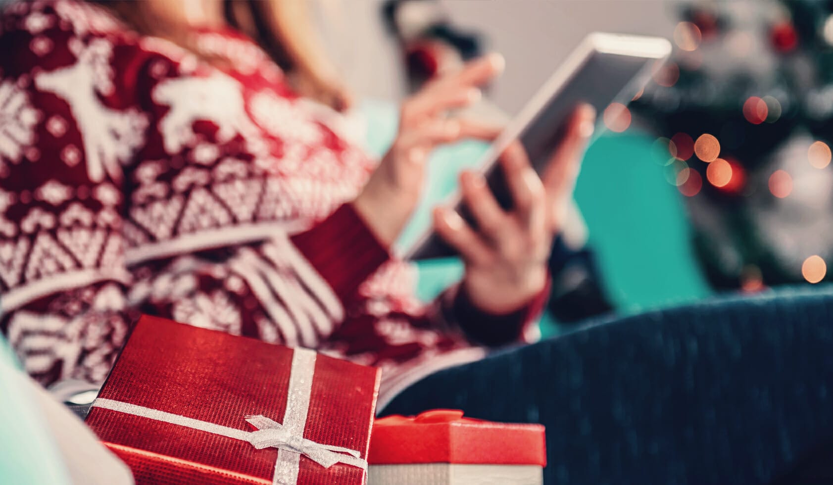 Woman wearing a holiday sweater and online holiday shopping on her tablet.