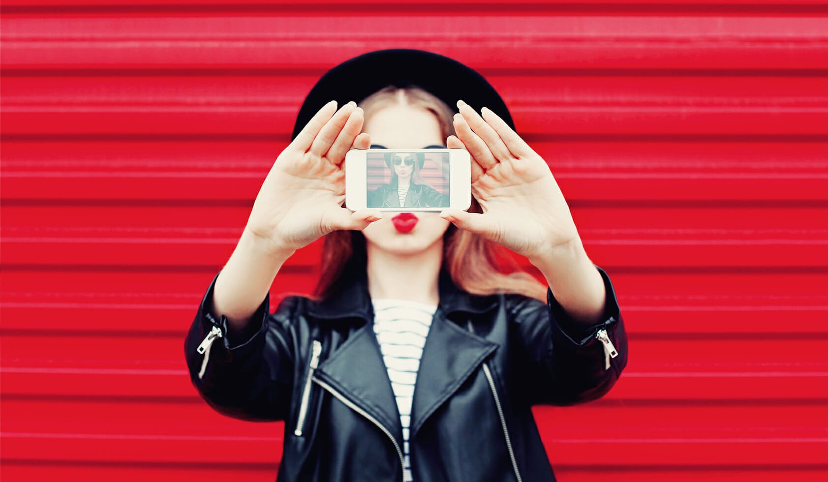 A female influencer holding her phone taking an selfie for social media.